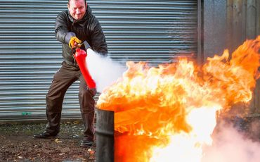 A man using a carbon dioxide extinguisher to fight a fire.