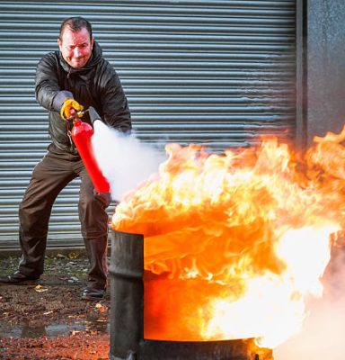 A man using a carbon dioxide extinguisher to fight a fire. A man using a carbon dioxide extinguisher to fight a fire.