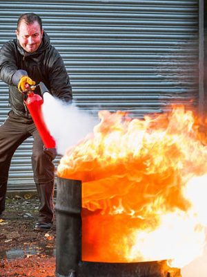 A man using a carbon dioxide extinguisher to fight a fire.
